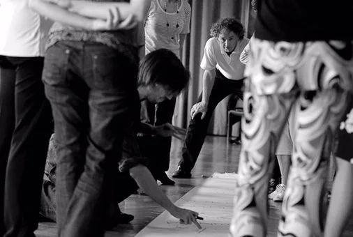 Shawn Koppenhoefer crouches on the floor and shows large dance-notation markings to a group at MuSaCa in Geneva